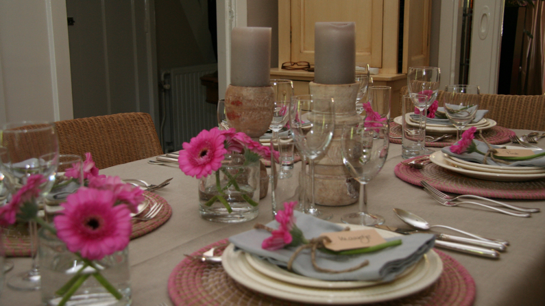 Feestelijk gedekte tafel met roze gerbera's en kaarsen