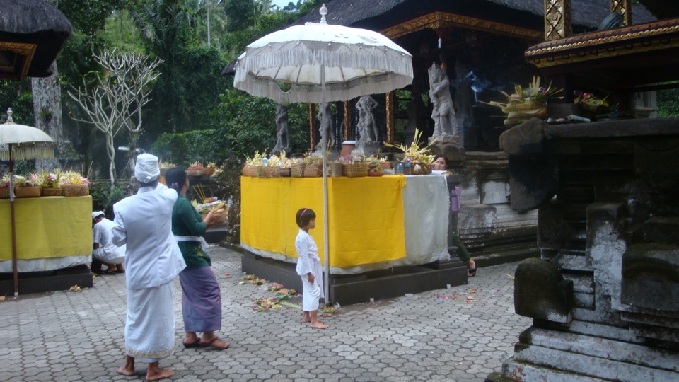 Tempelceremonie op Bali: mensen in witte kleding bij een met offers versierd altaar onder een witte parasol