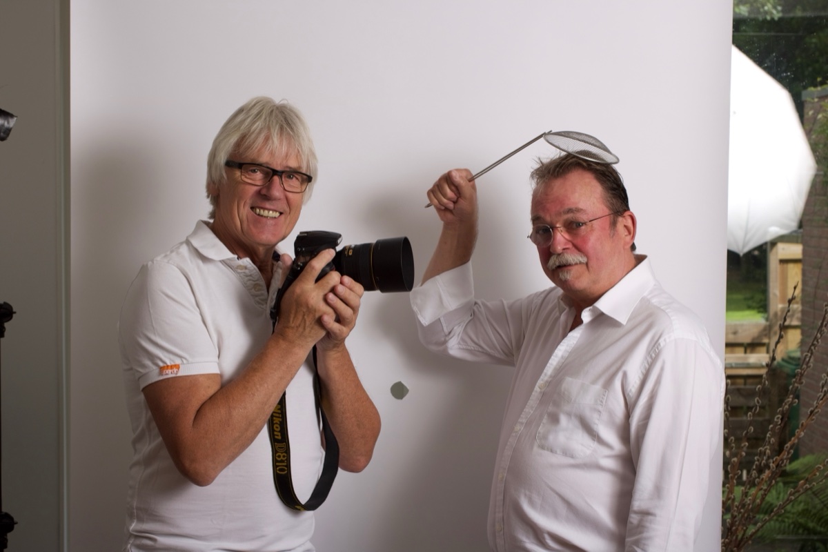 Hans Bakema fotografeert lachend terwijl Rob van Gasselt poseert met een zeef boven zijn hoofd
