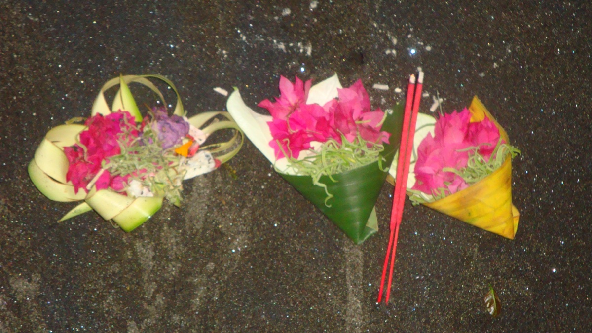 Offertjes met bloemen en wierook op de grond, voor de Buta Kala