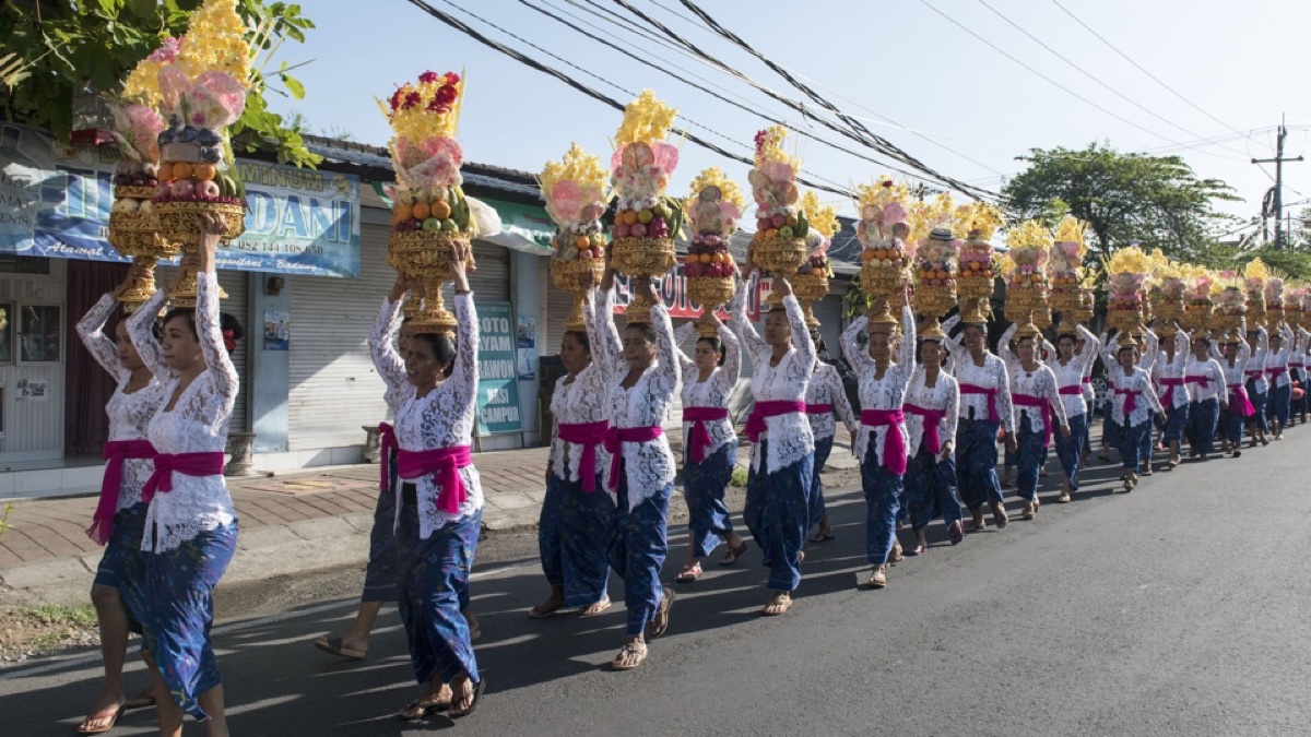 Lange rij vrouwen met offergaven op het hoofd op weg naar de tempel